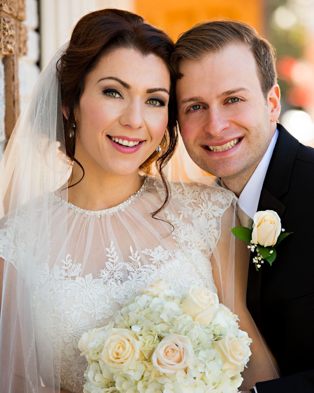 The bride and groom are posing for a picture and the bride is holding a bouquet of white roses