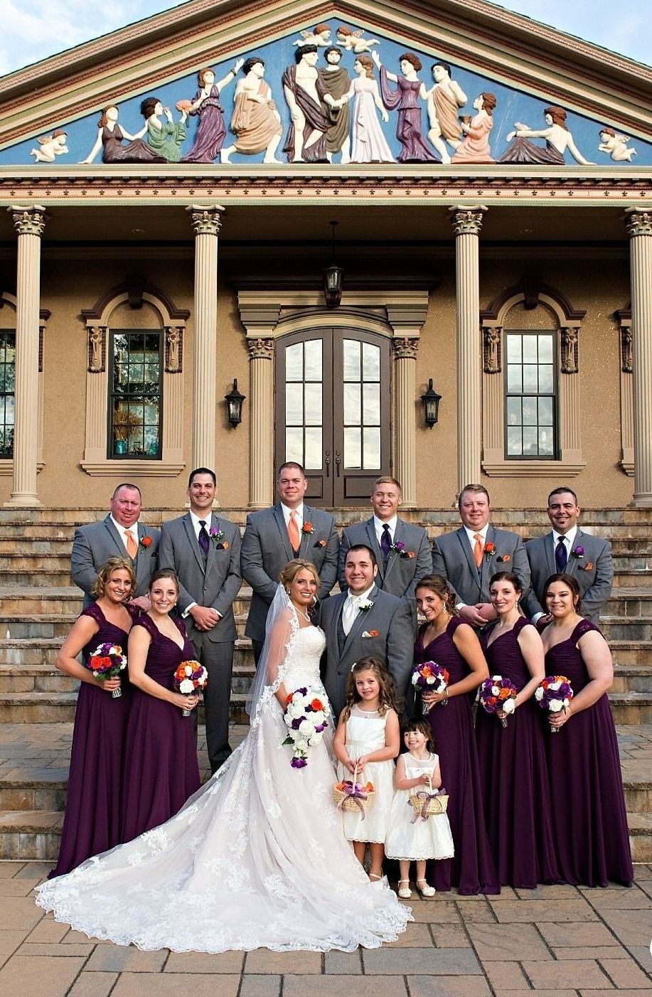 A bride and groom are posing for a picture with their wedding party in front of a building.