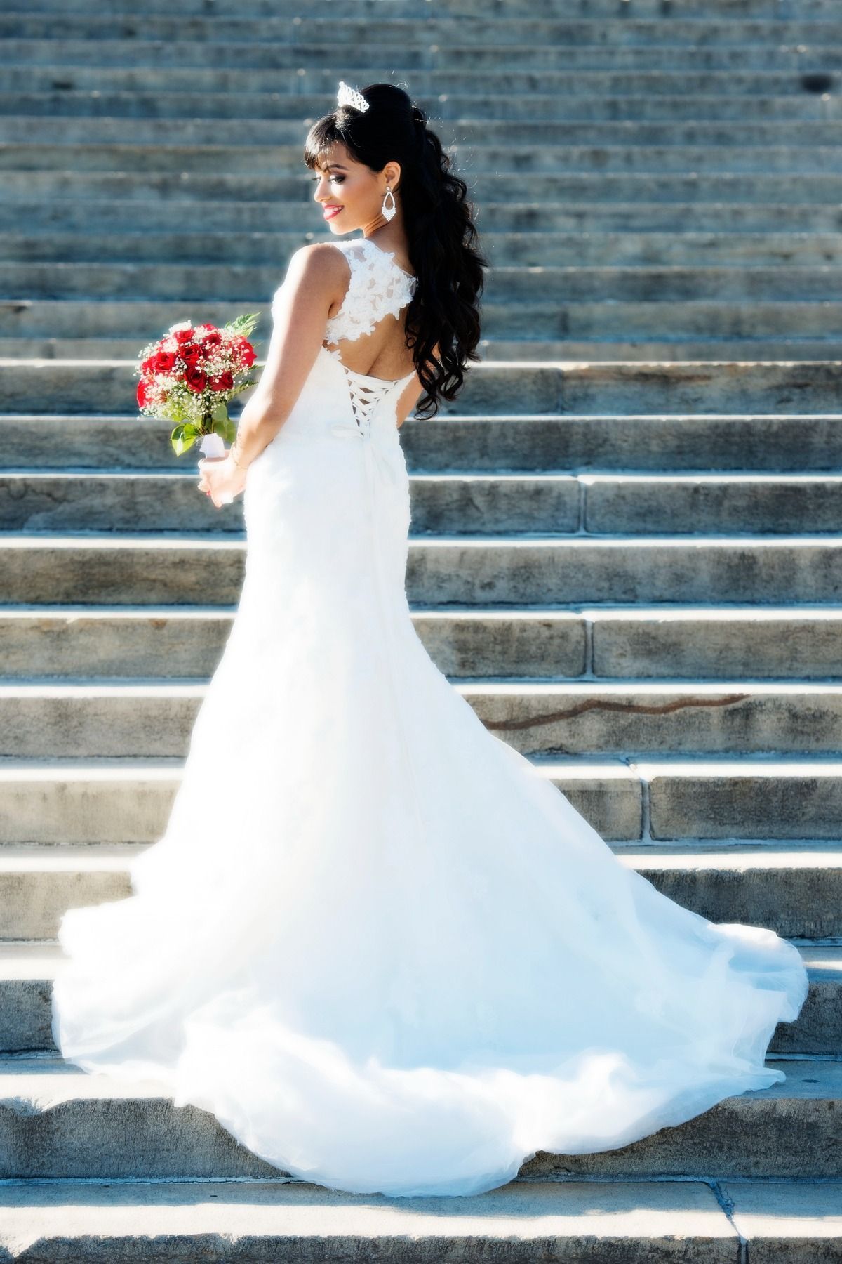 A woman in a wedding dress is standing on a set of stairs holding a bouquet of flowers.