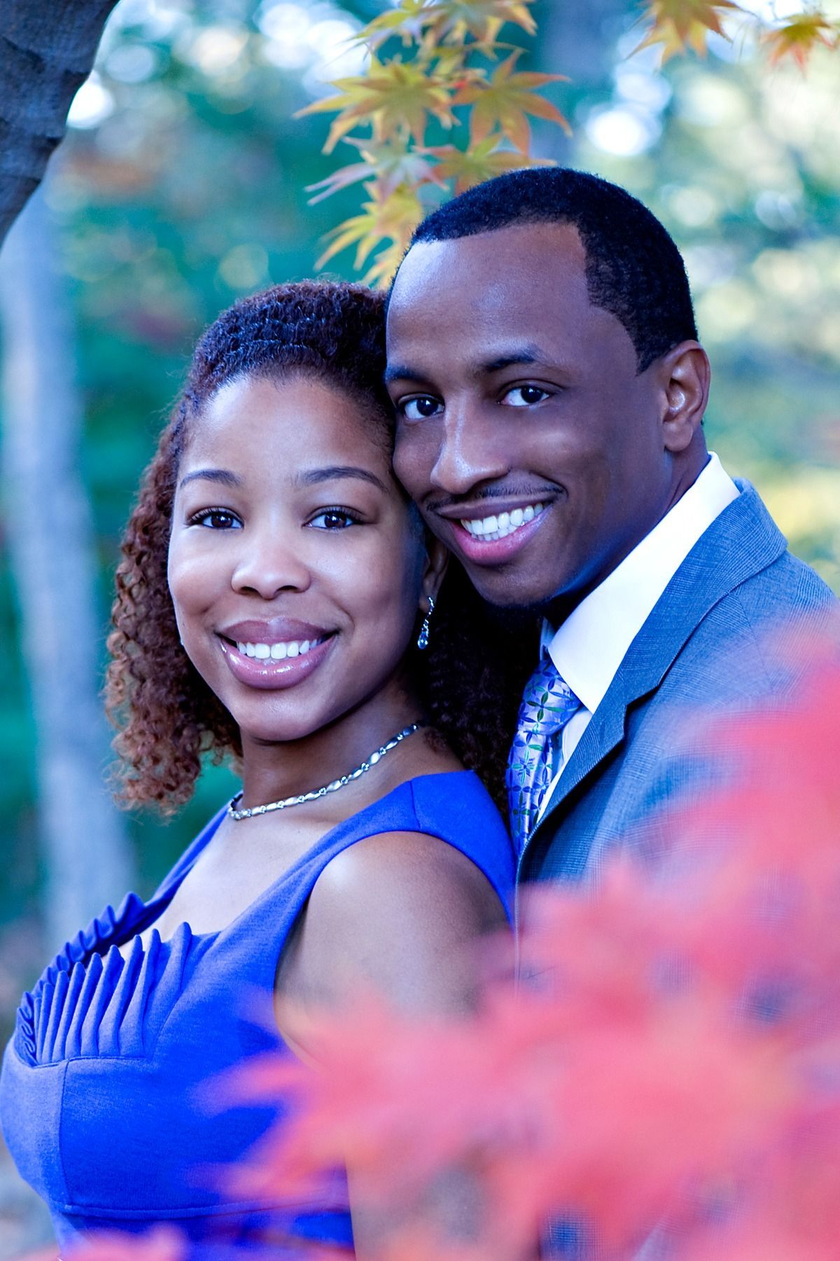A man and a woman are posing for a picture and the woman is wearing a blue dress