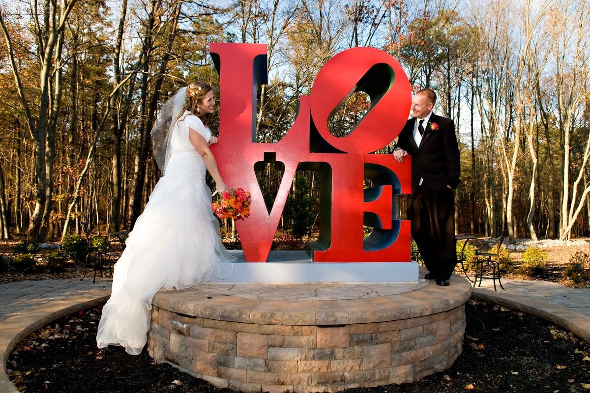 A bride and groom pose in front of a large red love sign.