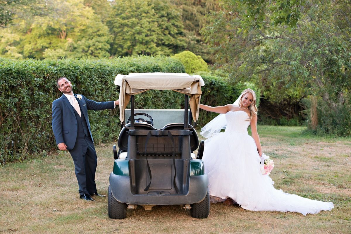 A bride and groom are posing for a picture next to a golf cart.