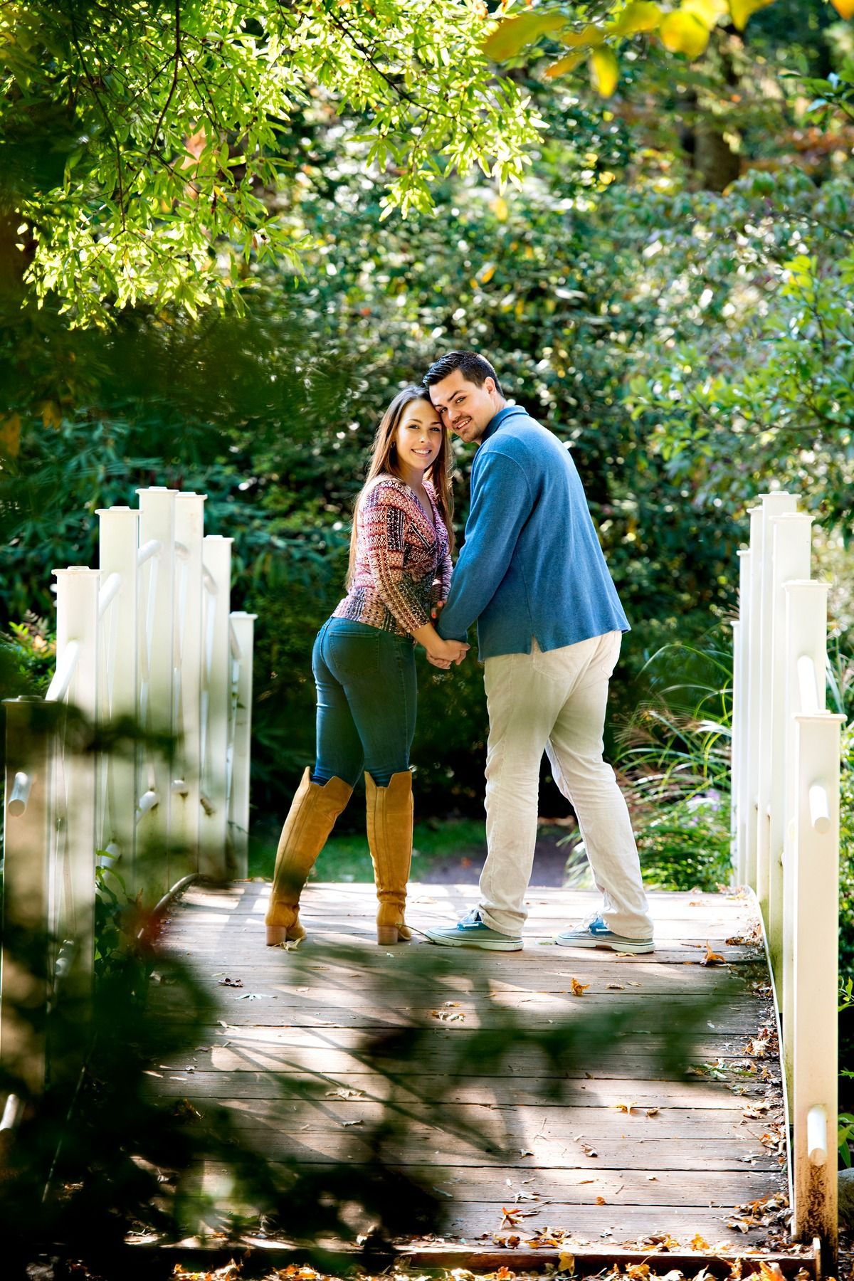 A man and a woman are standing on a wooden bridge holding hands.