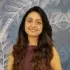 A woman with long hair is smiling in front of a wall with feathers on it.
