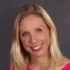 A woman with blonde hair is smiling in front of a painting