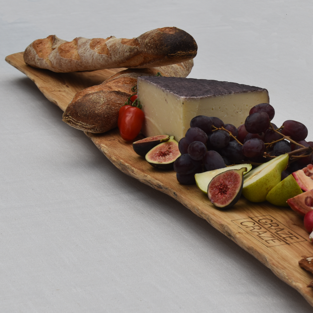 A wooden grazing board with bread grapes figs and cheese on it