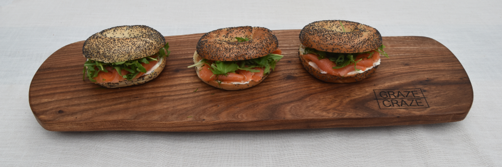 Three smoked salmon bagels sitting on a wooden grazing board.