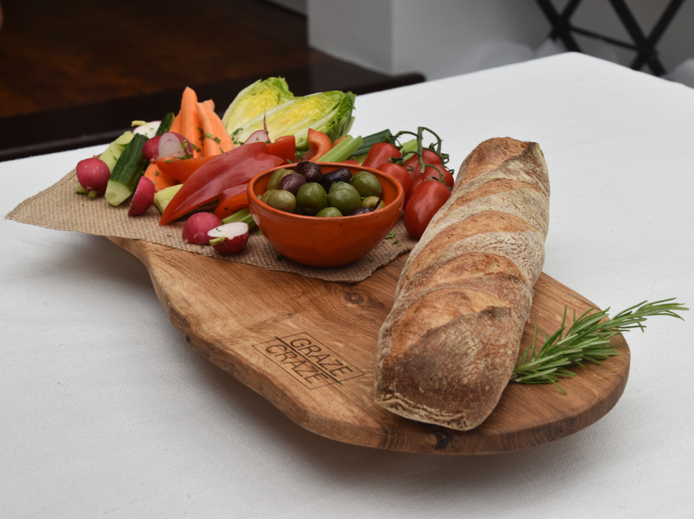 A wooden grazing board with vegetables and bread on it