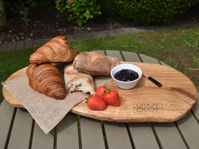 A wooden grazing board with croissants , strawberries and jam on it.