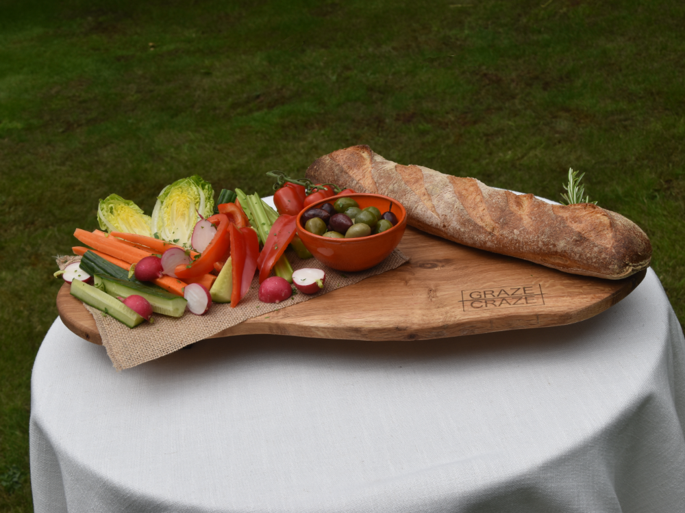 A wooden grazing board filled with vegetables and bread on a table.