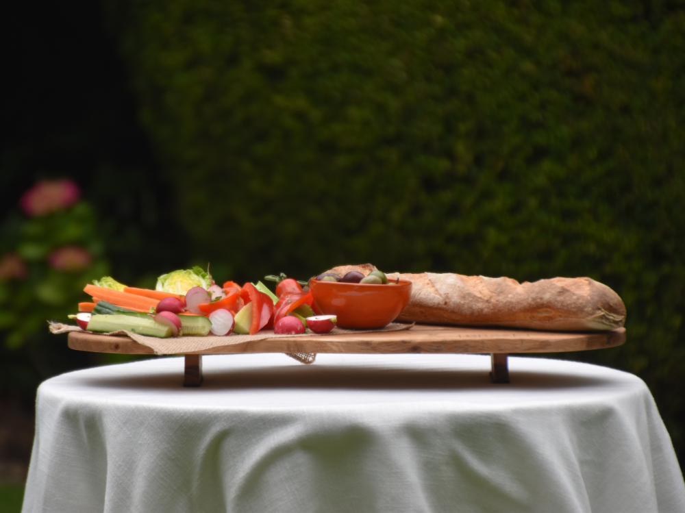 A wooden grazing board filled with vegetables and bread on a table.