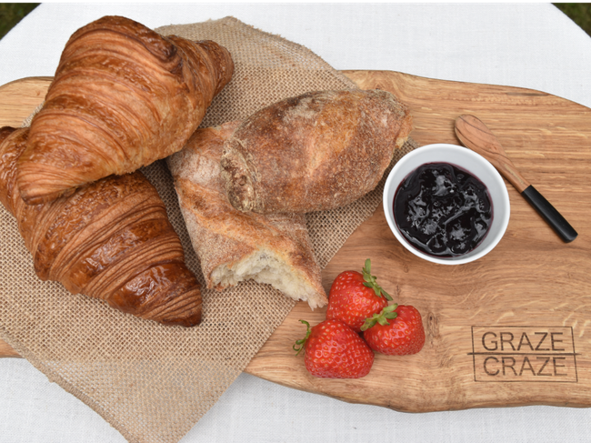 A wooden grazing board with a bowl of jam, strawberries and croissants on it.