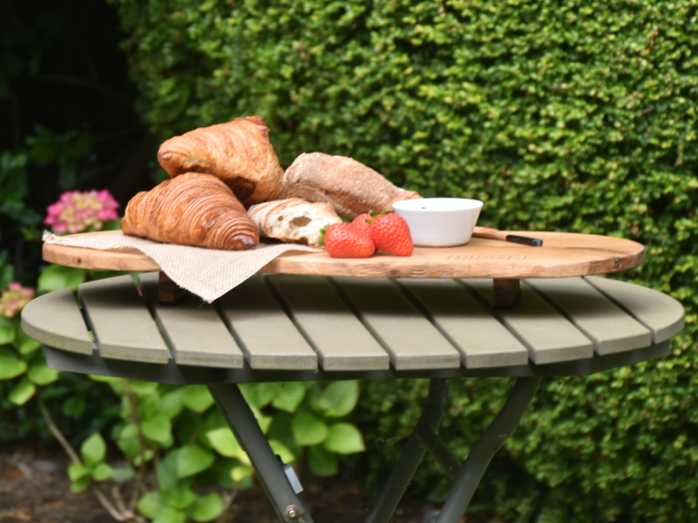 A wooden grazing board with croissants and strawberries on it, sitting on a table 