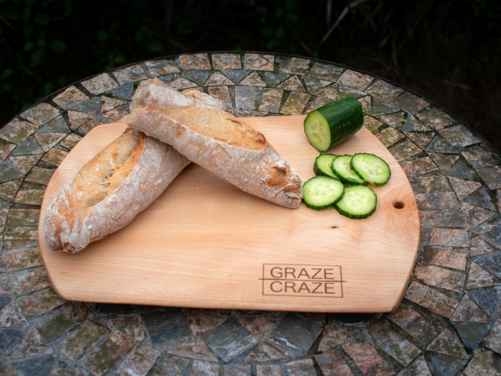 A wooden chopping board with bread and cucumbers on it.