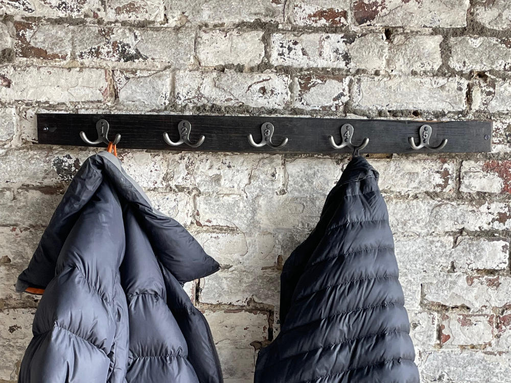 Two coats are hanging on a rack against a brick wall.