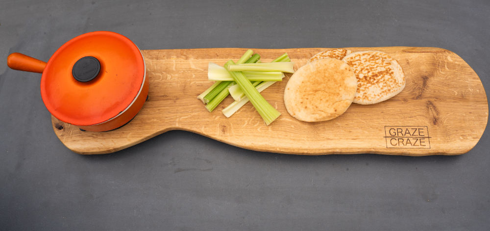 A wooden grazing board with bread , celery and a casserole pot on it.