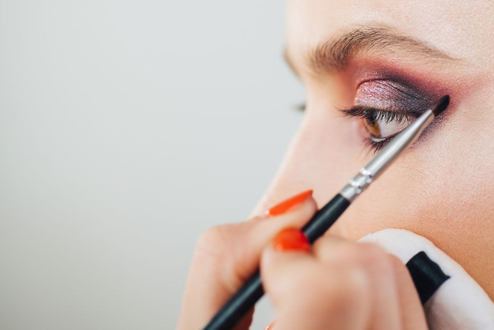 A woman is applying eye shadow to her eye with a brush.