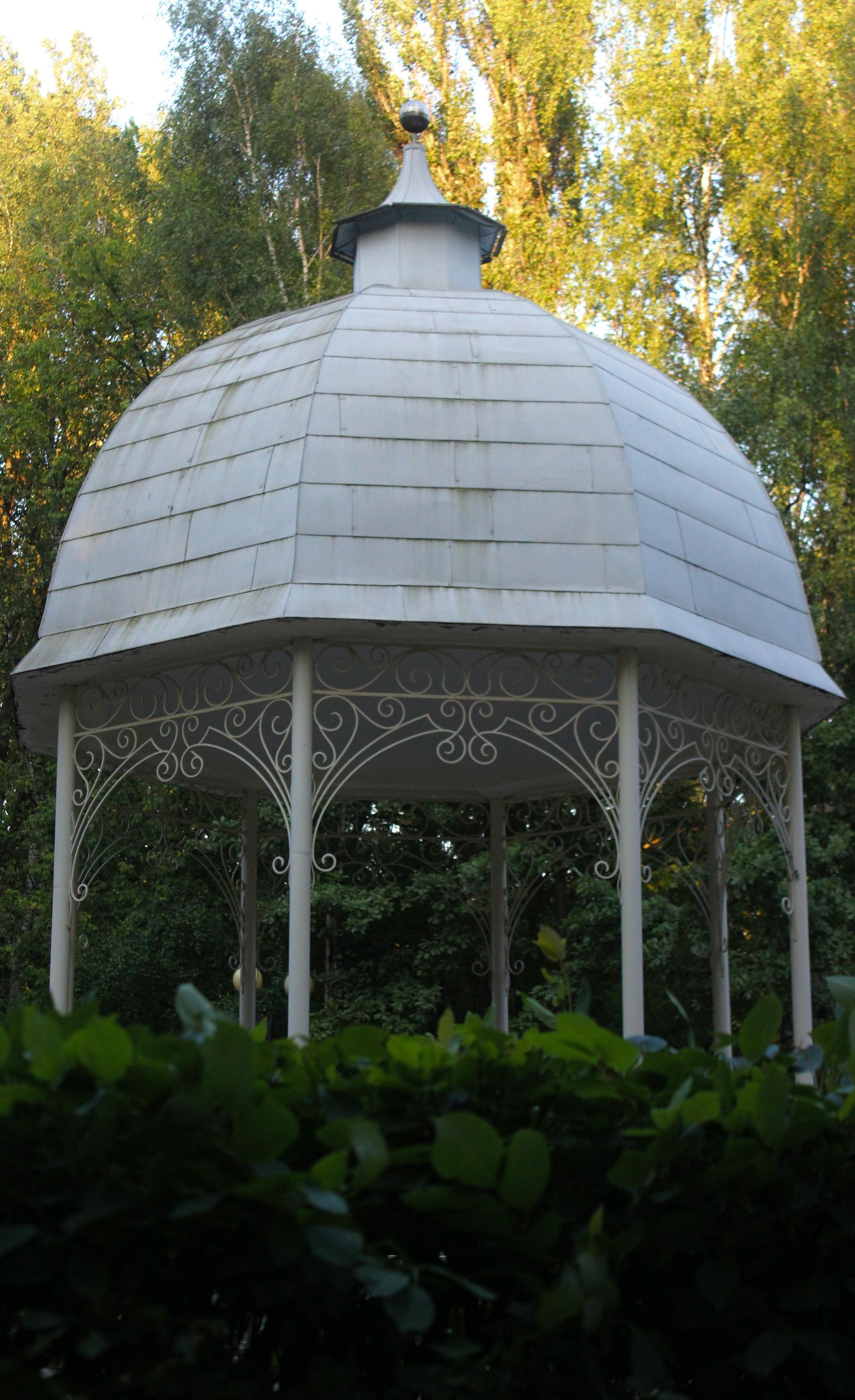 White gazebo in a garden, topped with a dome-shaped roof.