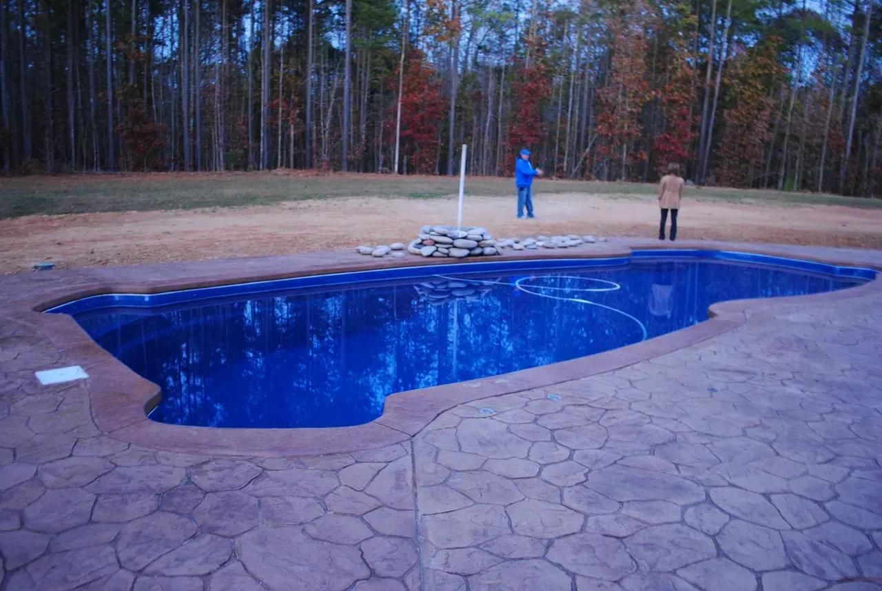 Two people are standing next to a large blue swimming pool.