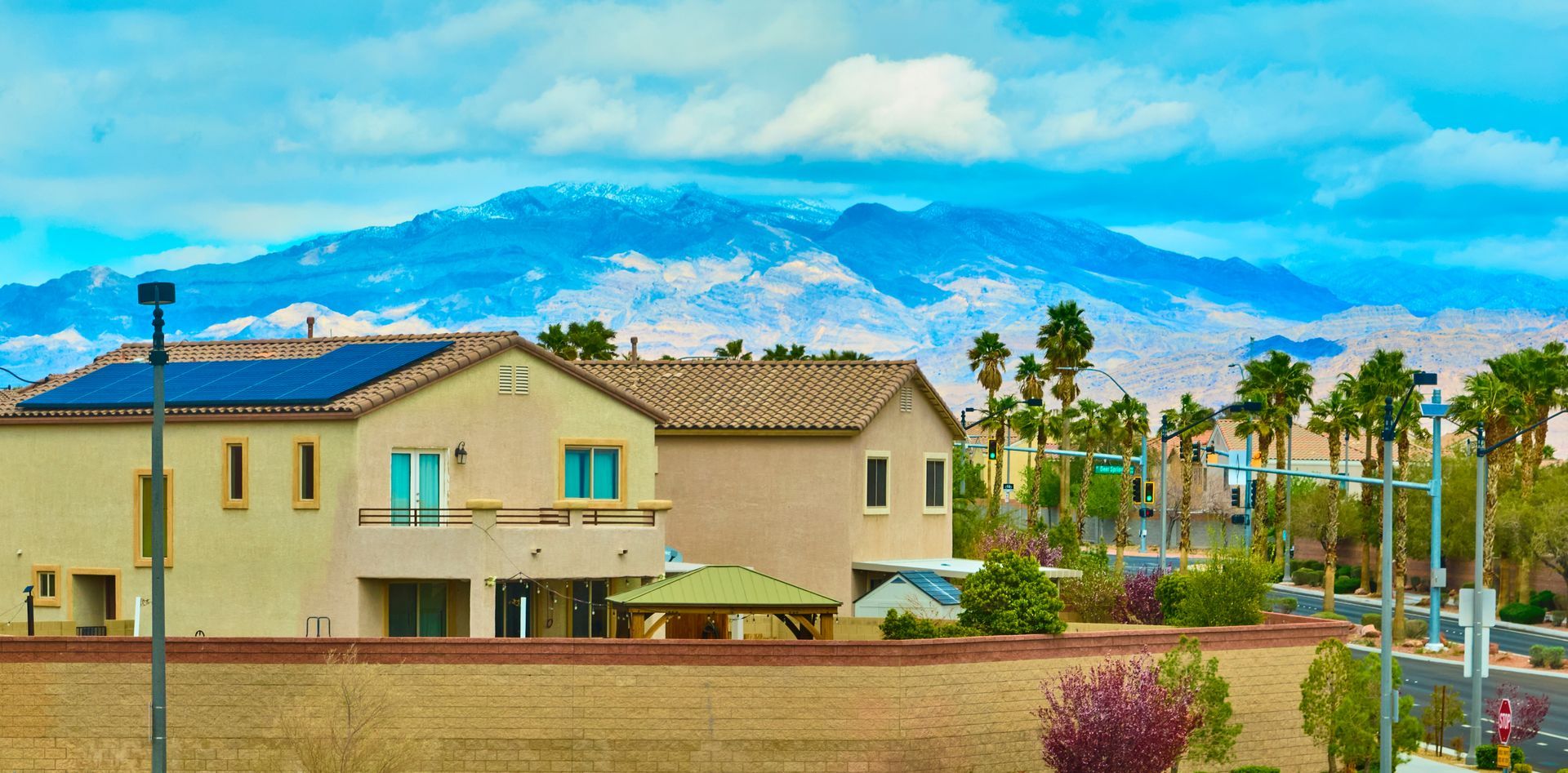 Houses with solar panels, palm trees, and a mountain range in the background under a blue sky.