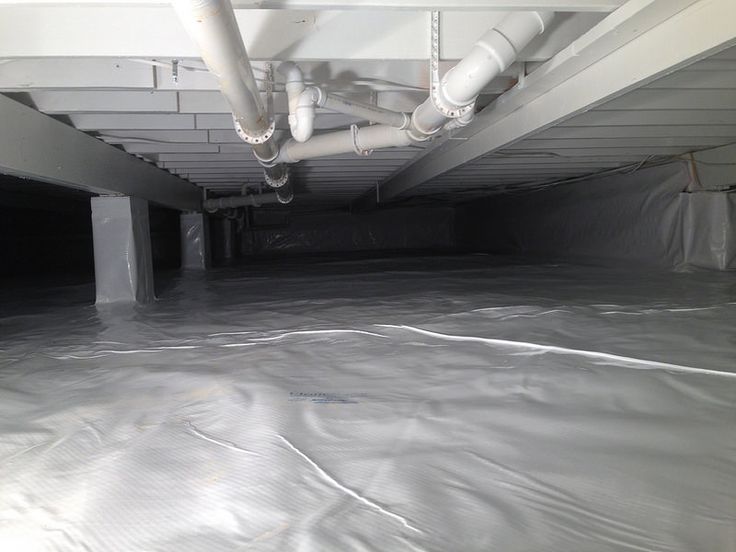 Man inspecting a foundation vent on a house. He kneels, looking closely at the opening, with the vent door propped open on the ground.