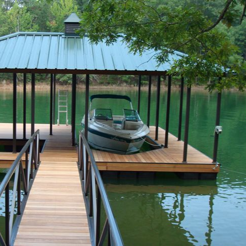Sunset over a pier with a weathered wooden structure, a boat, and calm water reflecting orange and blue sky.
