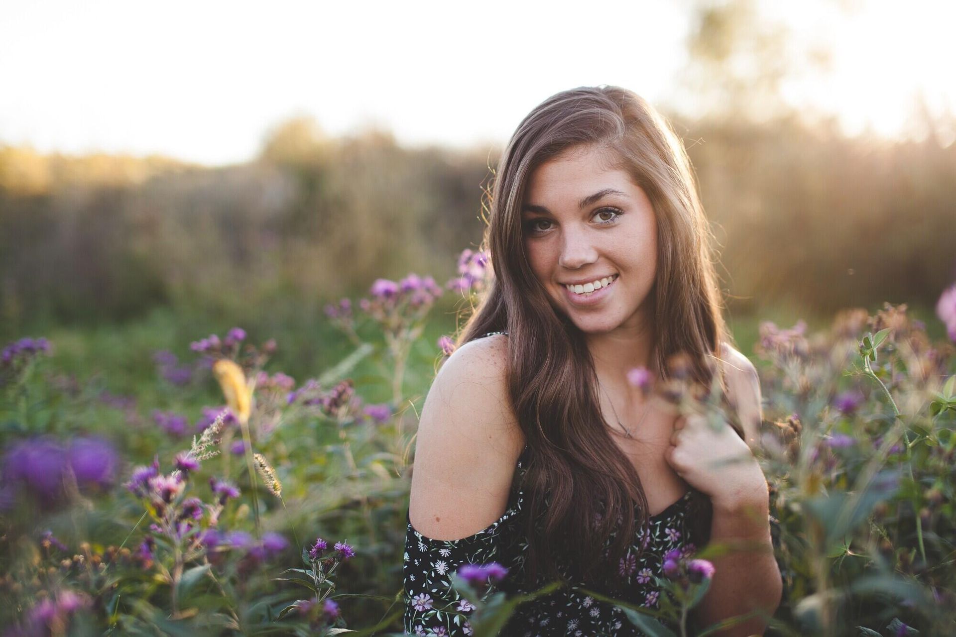 A young woman is sitting in a field of purple flowers.