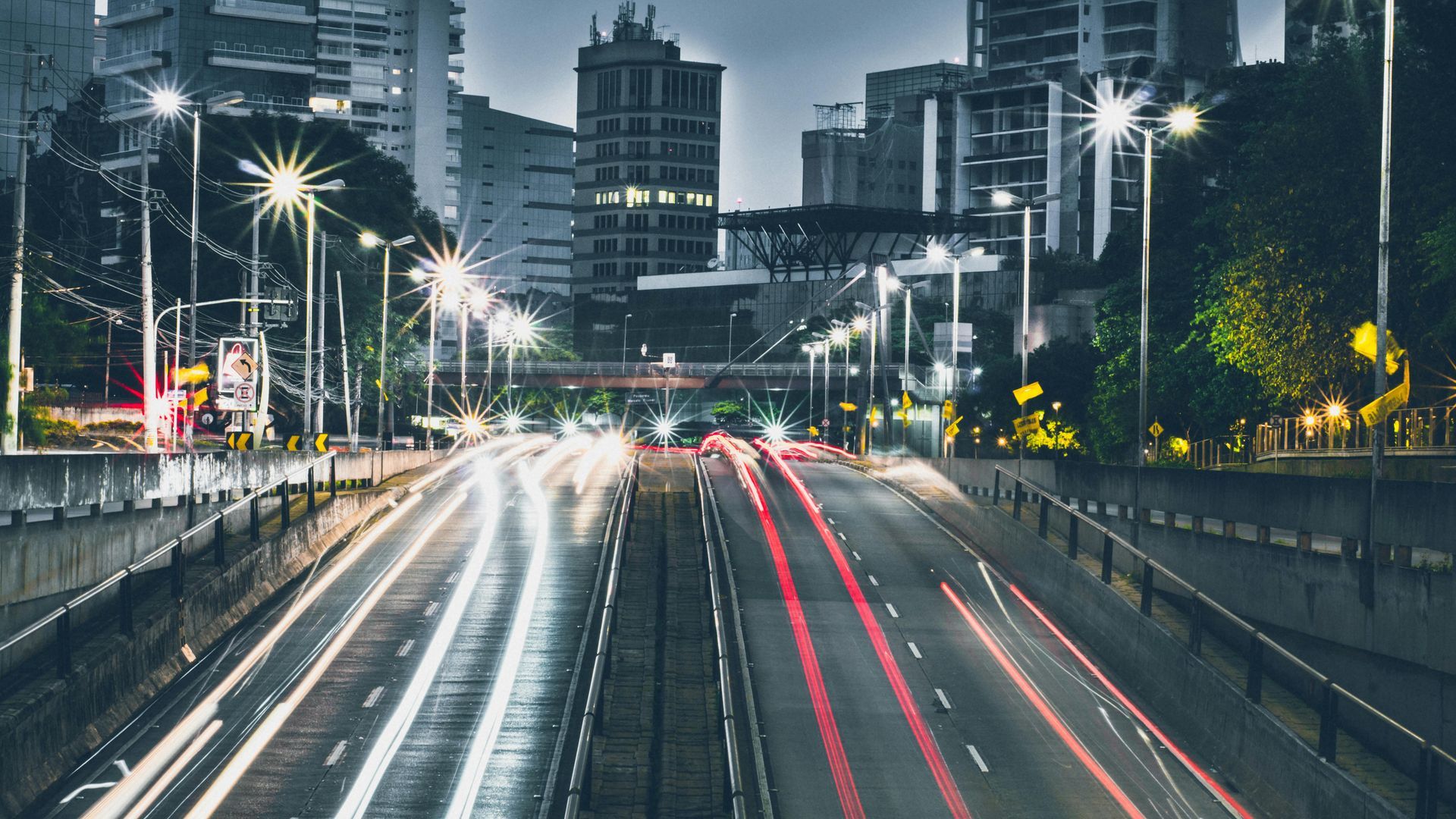 Highway at night with light trails from moving cars and city lights in the background.
