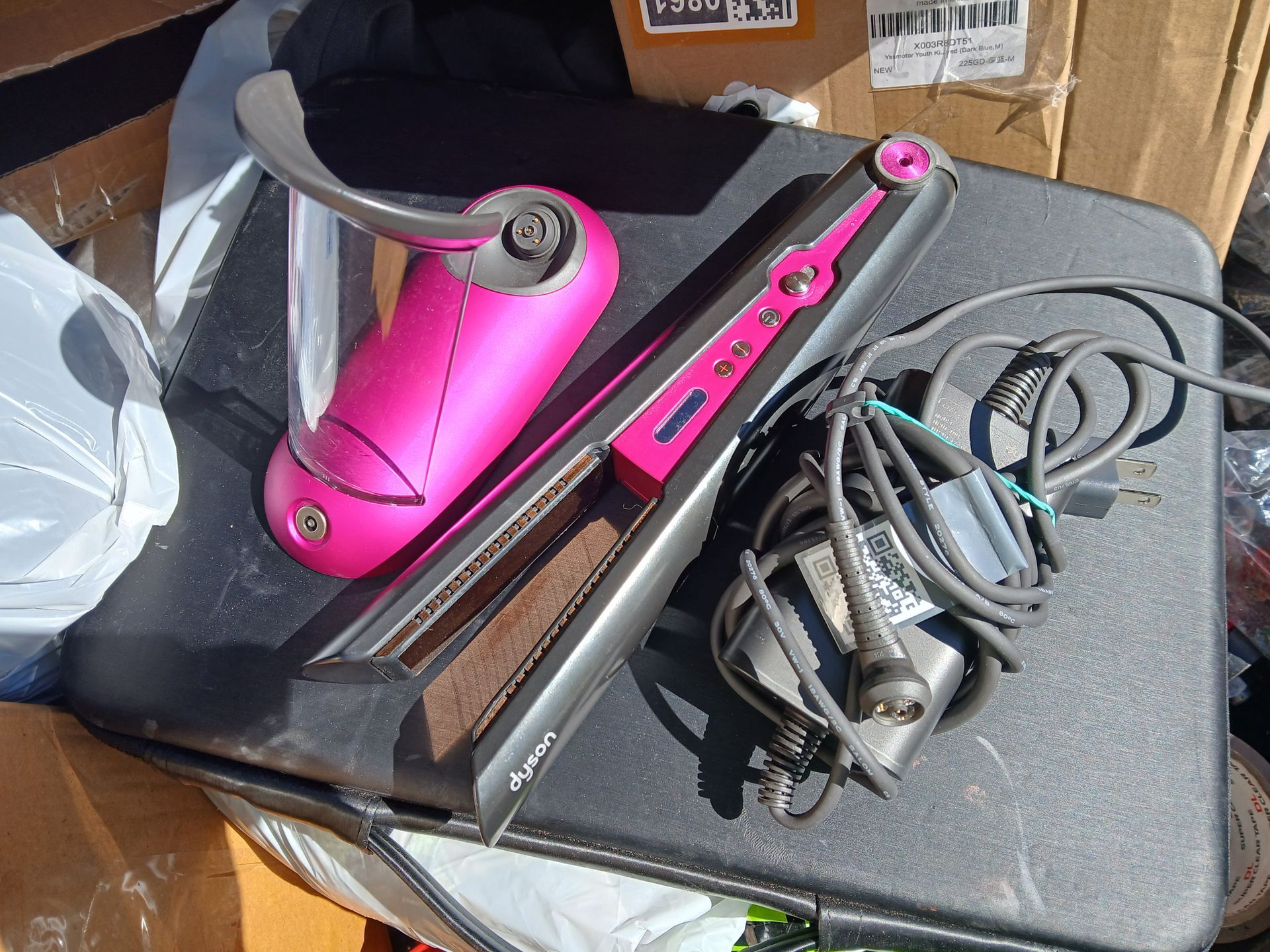Pink and black hair straightener with a pink hair dryer on a black surface.