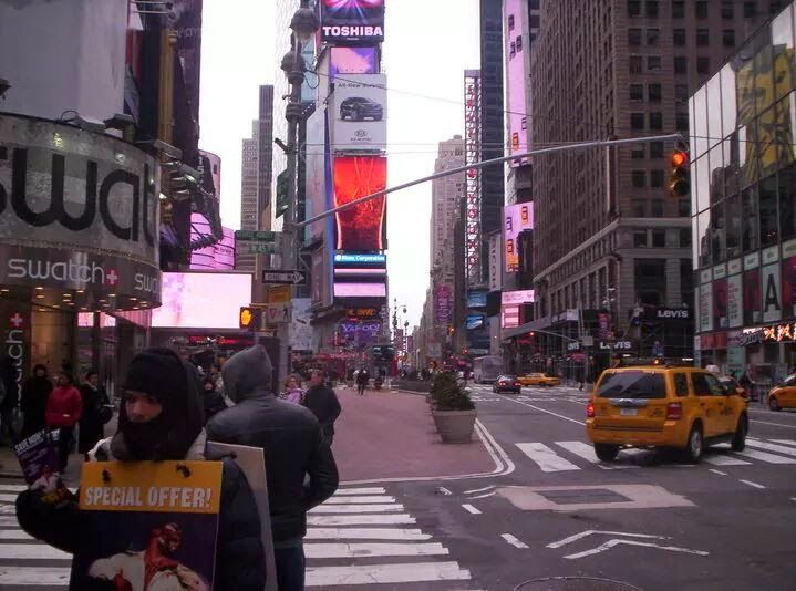 Times Square, New York City. Bright billboards and yellow taxis fill the street. People on crosswalk.