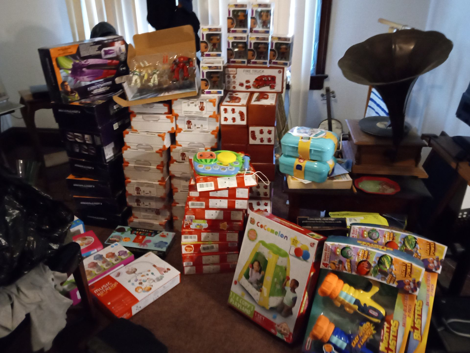 Piles of boxed toys and gifts in a room, including Funko Pops, a gramophone, and wrapping paper.