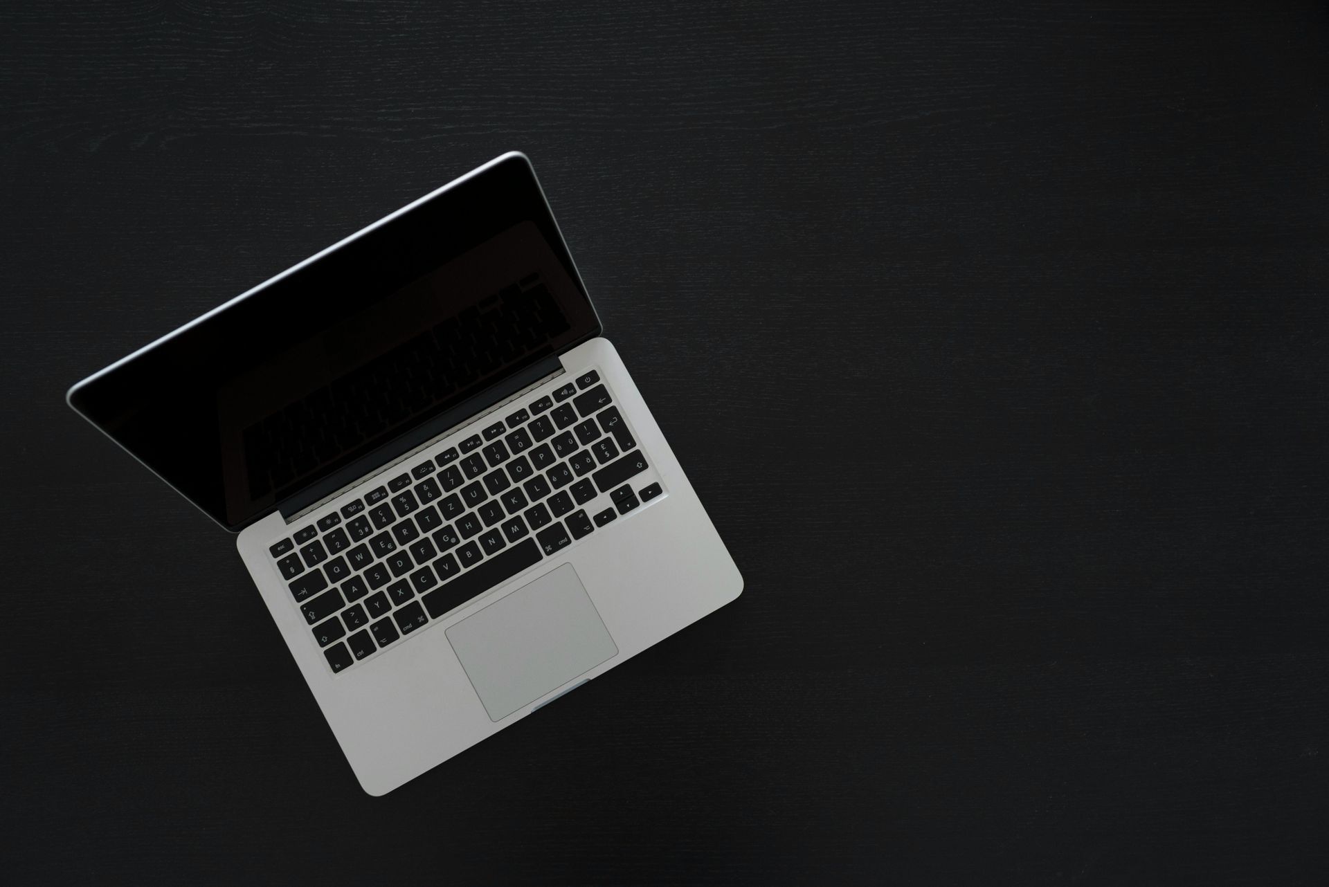 Laptop on a black surface; the screen is open, revealing a keyboard and trackpad.