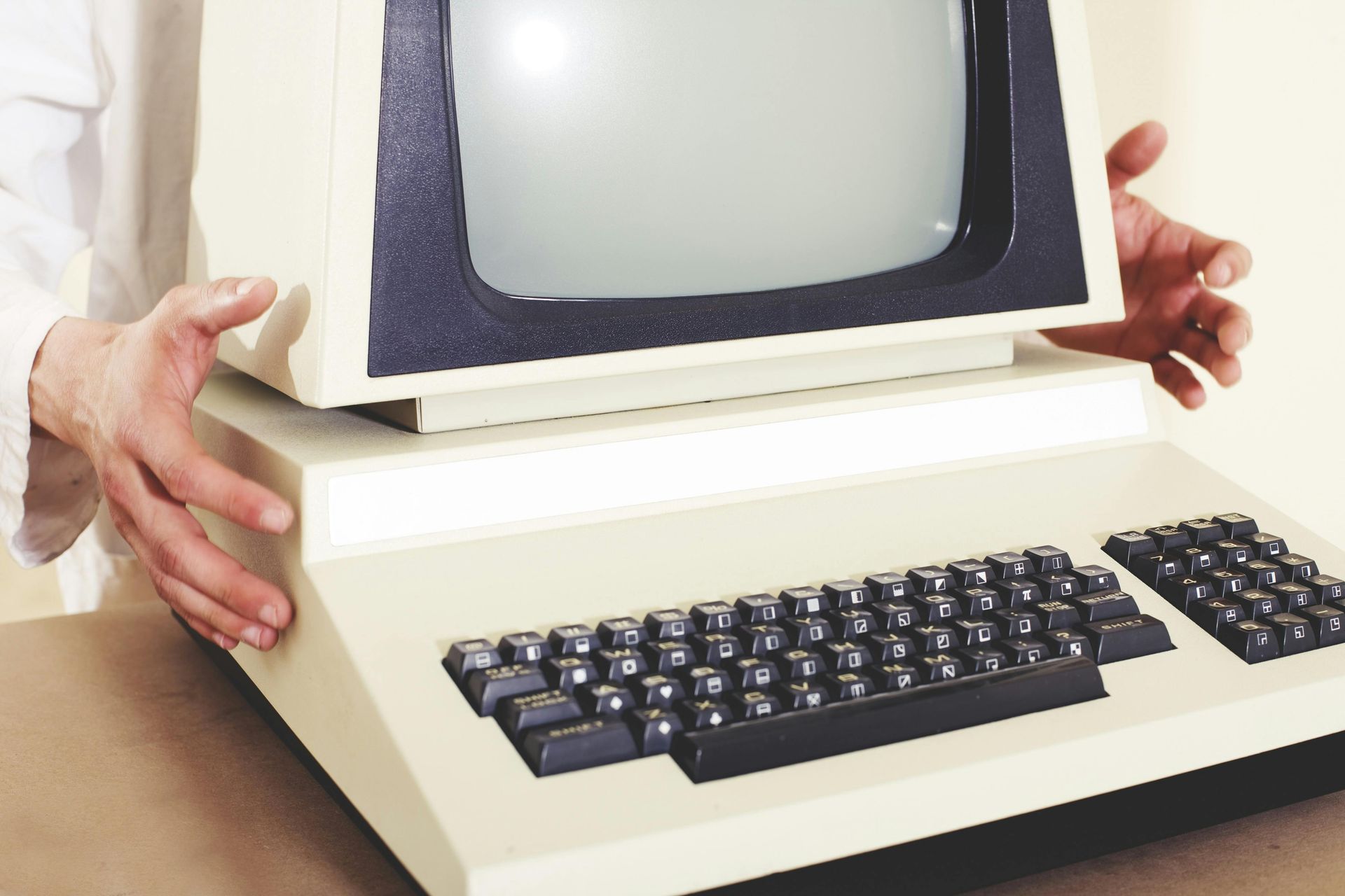 Person holding an old beige computer with a black screen and keyboard.