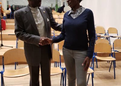 A man in a suit shaking hands with a person in a sweater and jeans, indoors.PLO Lumumba