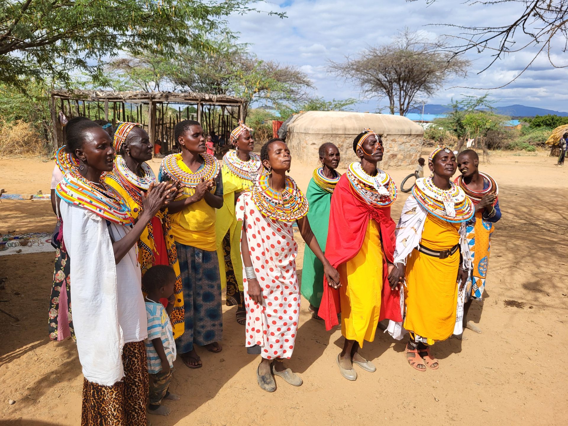 A group of Samburu women in colorful clothing stand outdoors, looking upward. Educultural Travel
