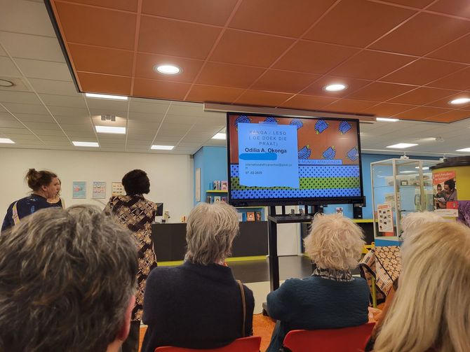 People watching a screen displaying a pixelated video game in a colorful room. Two women stand near the screen.