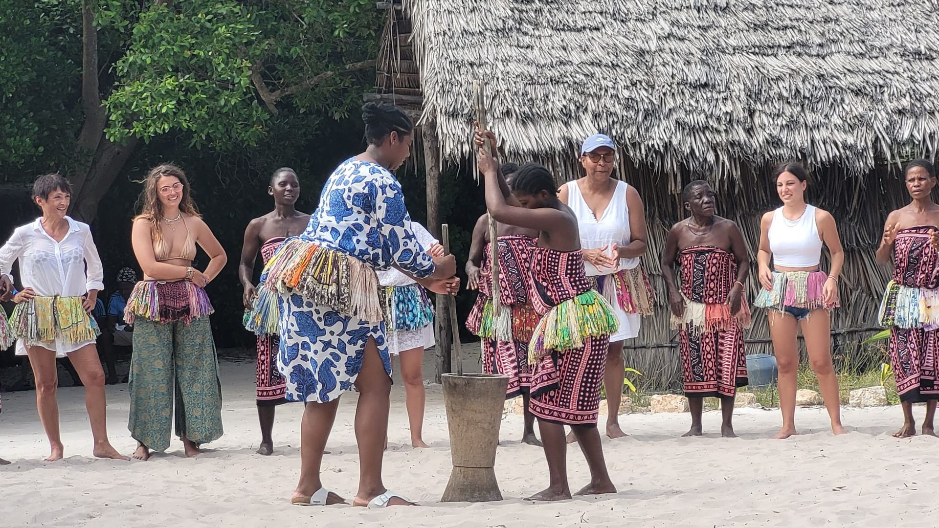 People watching a woman pound with a mortar and pestle outside a hut. Watamu. Educultural Travel