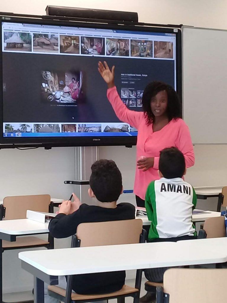 The teacher points to the classroom screen; students are seated at their desks.  Discovering Africa in the classroom