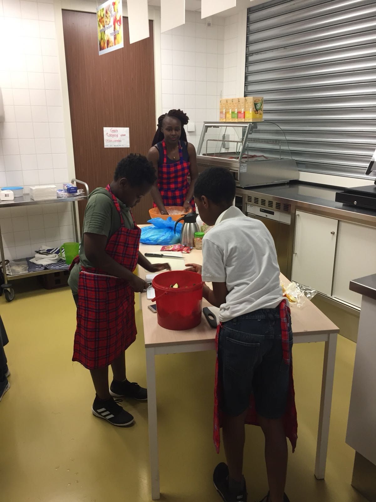 Three people wearing aprons in a kitchen prepare food at a table; a woman in the background.  Discovering Africa in the classroom