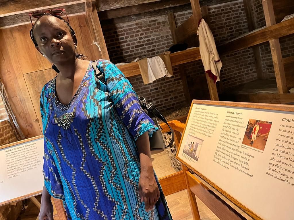 A woman in a blue dress stands in a room with wooden beams and signs.