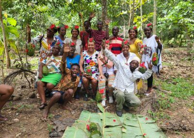 A group of people in a forest pose with raised hands, wearing floral headbands. They sit on a hillside with foliage. Educultural Travel