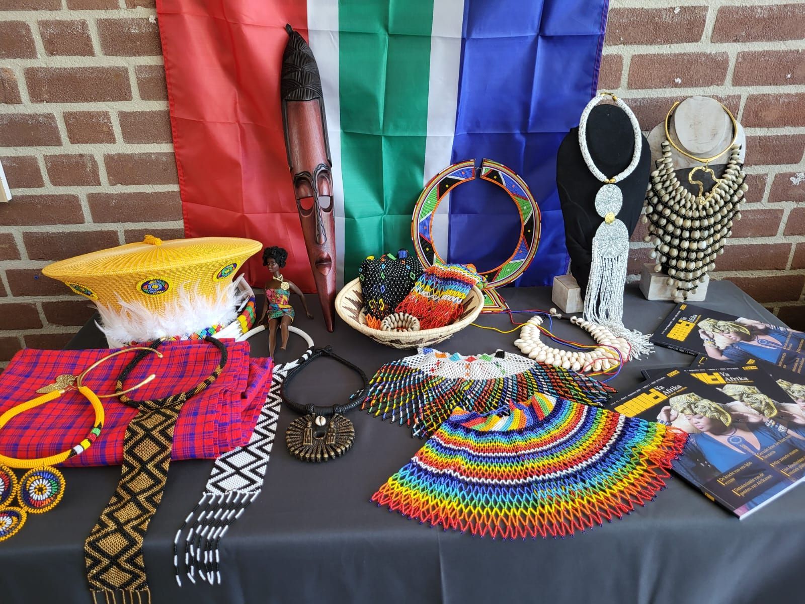 South African craft display: jewelry, flags, and carvings on a table in front of a brick wall.  Discovering Africa in the classroom