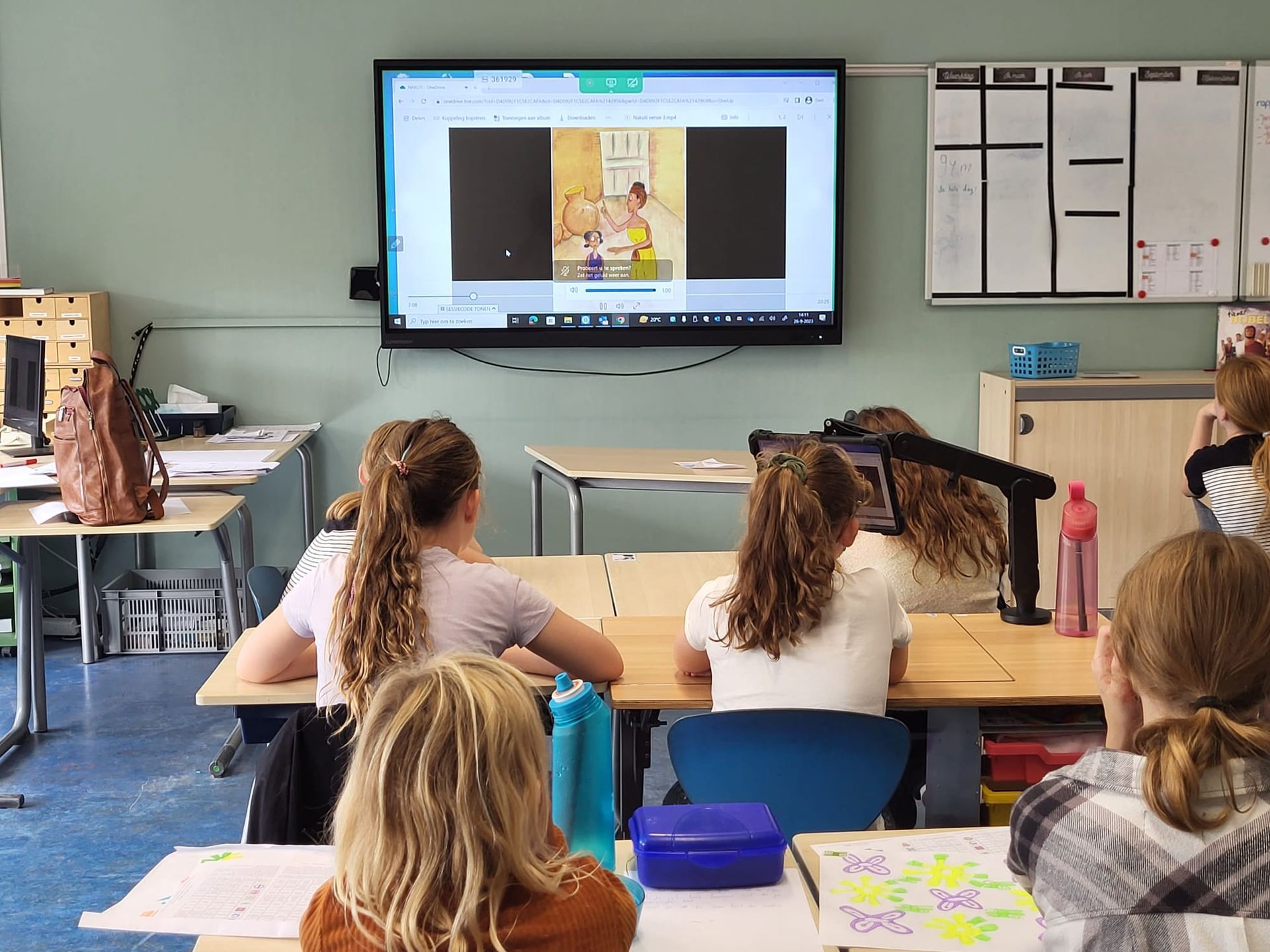 Children in a classroom are looking at a screen displaying a book. Desks and learning materials are visible.  Discovering Africa in the classroom