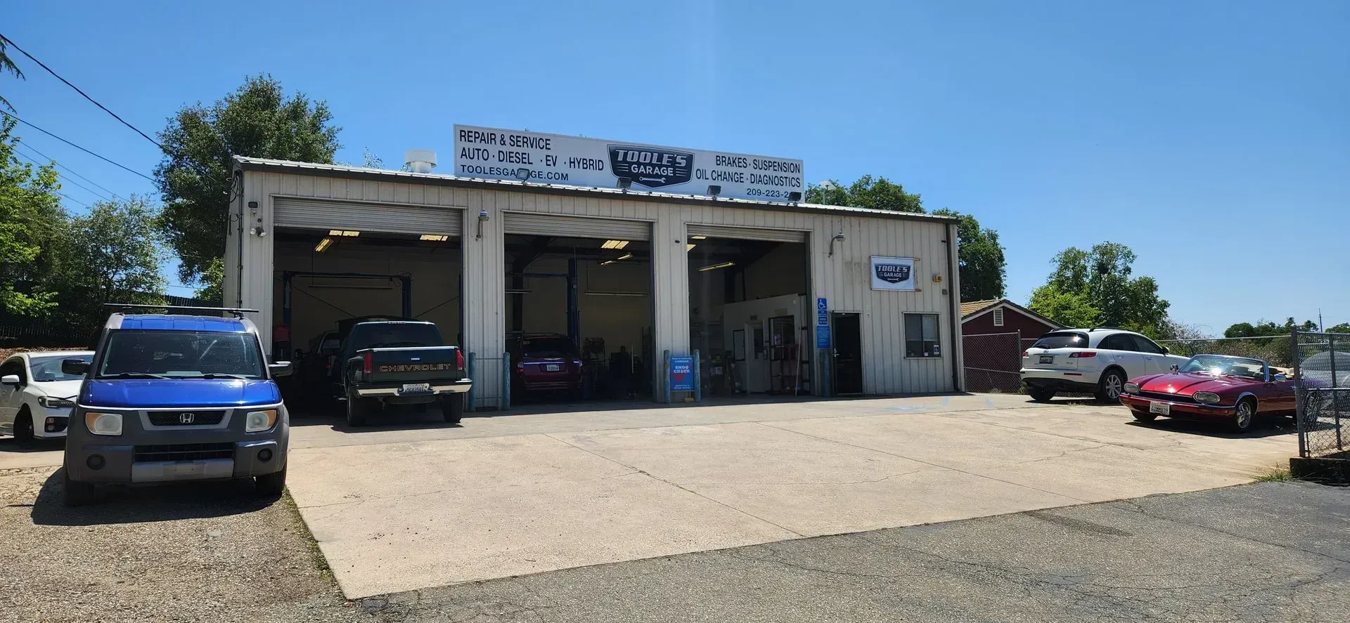 Auto repair shop with three garage bays. Cars parked in front. Sign on building. Sunny day.