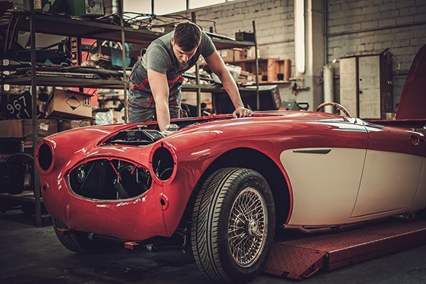 Mechanic working on the engine of a red and white classic car in a garage.