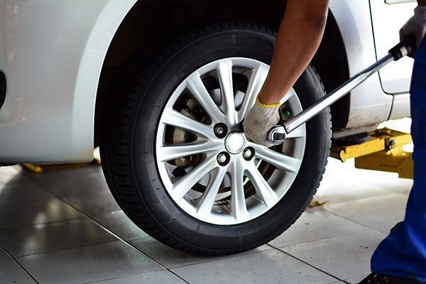 Person using a wrench to tighten lug nuts on a car tire in a garage.