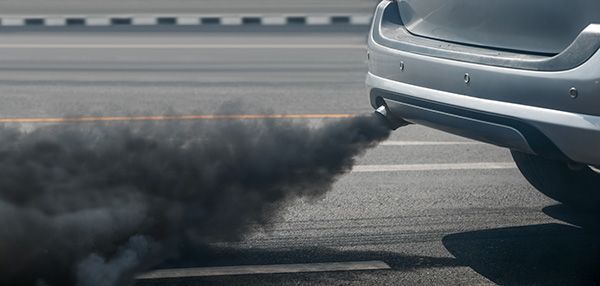 A car exhaust pipe emitting thick black smoke on a road.