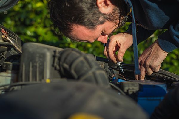 Man working on a car engine, inspecting parts. Outdoors, overcast.