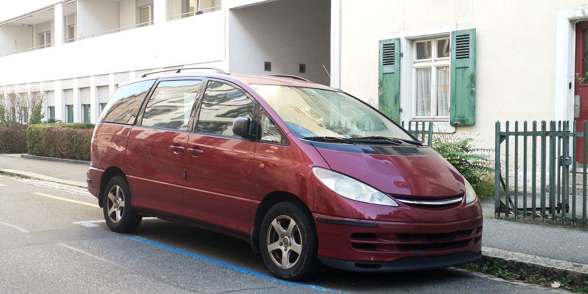 Red minivan parked on a city street, near a building with green shutters.