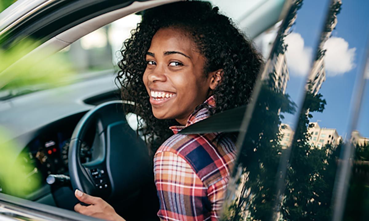 Woman smiling, sitting in car, looking over her shoulder.